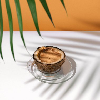 Coffee or cocoa drink in coconut shell cup under palm leaf. Exotic summer healthy treat concept. 
