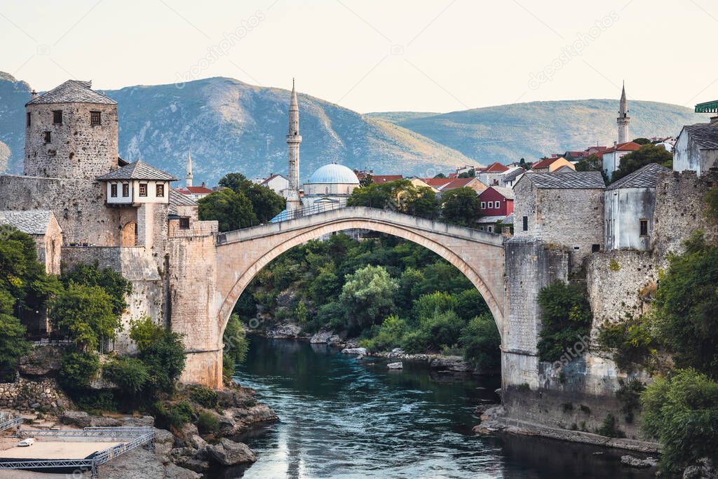 City of Mostar in Bosnia and Herzegovina with famous ottoman stone bridge, minarets and medieval buildings. Beautiful green river Neretva underneath.