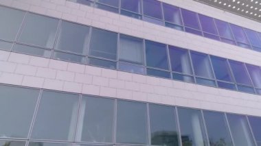 Beyaz cepheli bir iş kamerasının pencereleri sağa doğru hareket ediyor. Modern bir iş binasının pencere ve yansımaları