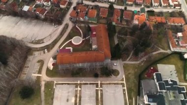 Bir ilkokulun ve boş oyun alanlarının yukarıdan aşağıya havadan çekilmiş görüntüsü. Kırmızı çatılar, kış günü.