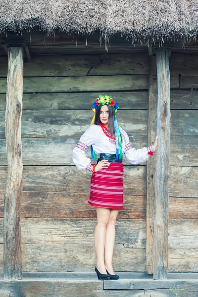 Woman wearing national ukrainian clothes near wooden hut — Stock Photo, Image