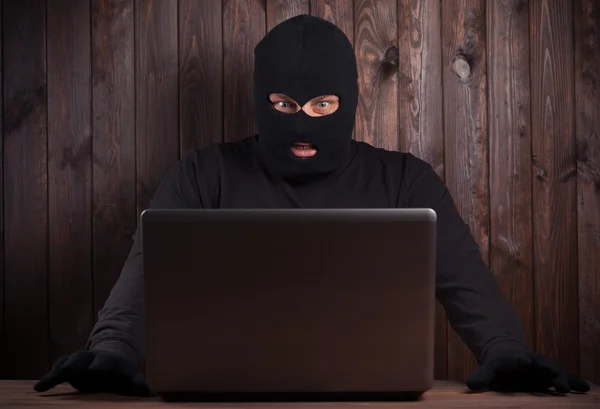 Хакер в балаклаве с компьютером — стоковое фото