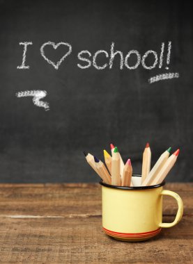 Ahşap masa ve tebeşir tahtası üzerinde bir kupa içinde Kalemler