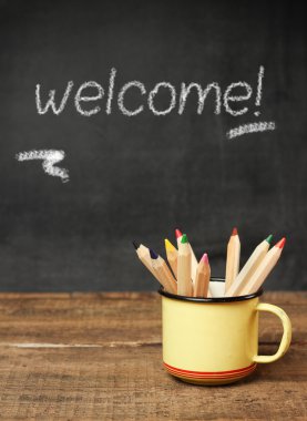 Ahşap masa ve tebeşir tahtası üzerinde bir kupa içinde Kalemler