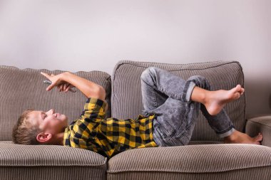 Ailesi ve arkadaşlarıyla konuşan sevimli bir çocuk telefonda video görüşmesi yapıyor, kanepede oturuyor. Evde kal, kilitle, sosyal uzaklık, karantina.