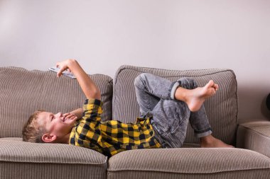 Ailesi ve arkadaşlarıyla konuşan sevimli bir çocuk telefonda video görüşmesi yapıyor, kanepede oturuyor. Evde kal, kilitle, sosyal uzaklık, karantina.