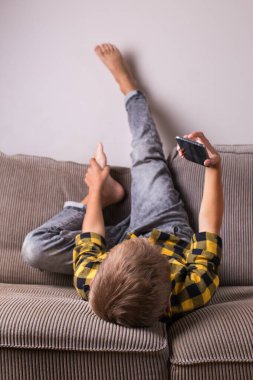 Ailesi ve arkadaşlarıyla konuşan sevimli bir çocuk telefonda video görüşmesi yapıyor, kanepede oturuyor. Evde kal, kilitle, sosyal uzaklık, karantina.