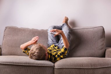 Ailesi ve arkadaşlarıyla konuşan sevimli bir çocuk telefonda video görüşmesi yapıyor, kanepede oturuyor. Evde kal, kilitle, sosyal uzaklık, karantina.