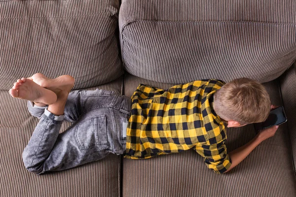 Cute smiling boy talking with family and friends, making video call on the phone, sitting on a couch. Stay at home, lockdown, social distancing, quarantine.