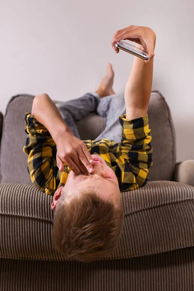 Cute smiling boy talking with family and friends, making video call on the phone, sitting on a couch. Stay at home, lockdown, social distancing, quarantine.