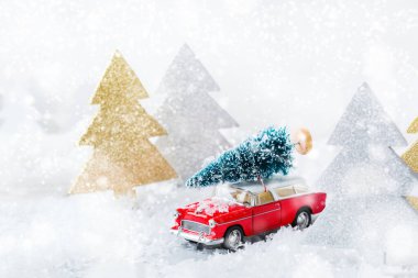 Yeni yıl tatili konsepti. Kar ormanında Noel ağacı taşıyan kırmızı oyuncak araba. Tebrik kartını şenlikli dekorasyonla kopyala