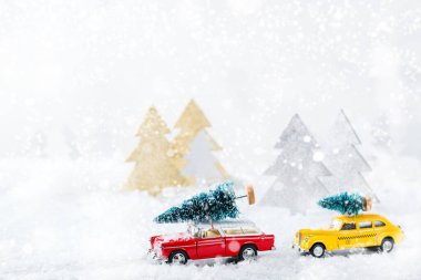 Yeni yıl tatili konsepti. Sarı oyuncak taksi ve kar ormanında Noel ağacı taşıyan kırmızı araba. Tebrik kartını şenlikli dekorasyonla kopyala