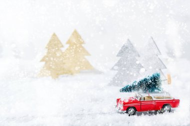 Yeni yıl tatili konsepti. Kar ormanında Noel ağacı taşıyan kırmızı oyuncak araba. Tebrik kartını şenlikli dekorasyonla kopyala