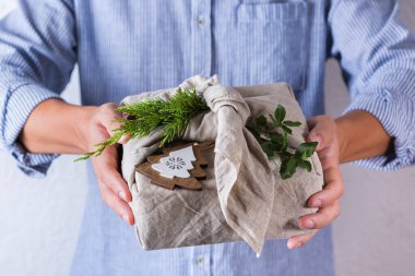 Yaratıcı sıfır noel konsepti. El yapımı hediye paketi veren eller çevre dostu geleneksel Japon tarzı furoshiki kumaşına sarılıyor.
