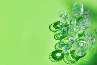 Durgun ve köpüklü su bardakları modayı takip eden güneşli, canlı, sert ve sert ışık ve yeşil arka planda gölgeler, açık havada, kopyalama alanı.