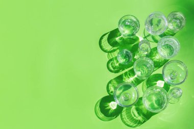 Durgun ve köpüklü su bardakları modayı takip eden güneşli, canlı, sert ve sert ışık ve yeşil arka planda gölgeler, açık havada, kopyalama alanı.