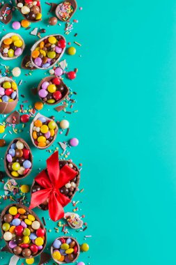 Turkuazda çikolatalı yumurta ve şekerli paskalya çerçevesi, yeşil, mavi arka plan. Boşluğu kopyala, üst görünüm, düz uzanma