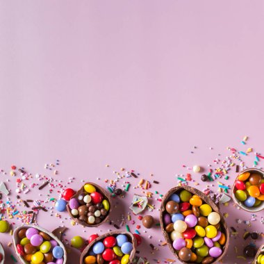 Pembe arka planda çikolatalı yumurta ve şekerli Paskalya çerçevesi. Boşluğu kopyala, üst görünüm, düz uzanma