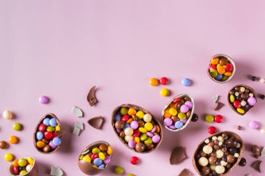 Pembe arka planda çikolatalı yumurta ve şekerli Paskalya çerçevesi. Boşluğu kopyala, üst görünüm, düz uzanma