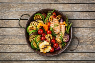 Mevsimlik, yaz yeme konsepti. Ahşap bir masada ızgara sebze ve tavuk göğsü. Üst görünüm düz arkaplan