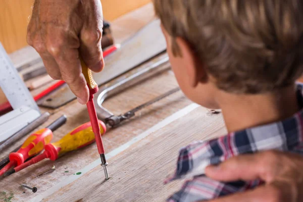 Дедушка учит мальчика работать на скамейке со столярными инструментами. — стоковое фото