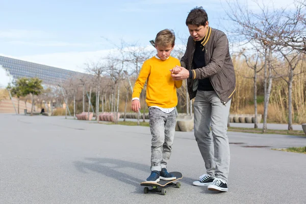 Papà sta insegnando a suo figlio a cavalcare uno skateboard, all'aperto — Foto Stock