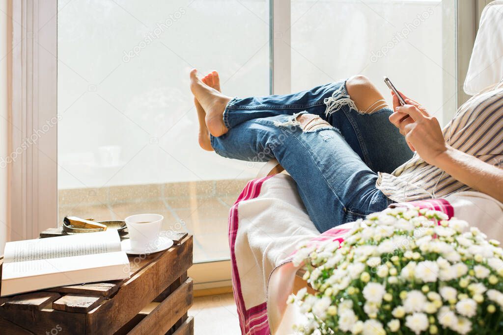 Young woman is relaxing at home, drinking tea, using phone