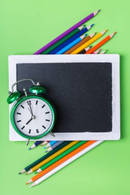 Renkli gökkuşağı kalemleri ve yeşil arka planda alarm saati