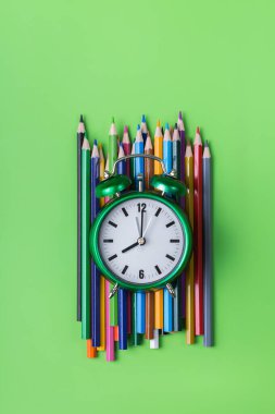 Renkli gökkuşağı kalemleri ve yeşil arka planda alarm saati