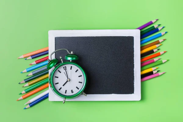 Renkli gökkuşağı kalemleri ve yeşil arka planda alarm saati — Stok fotoğraf