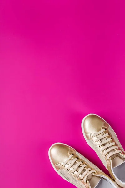 Par gyllene kvinnliga sneakers på rosa bakgrund — Stockfoto