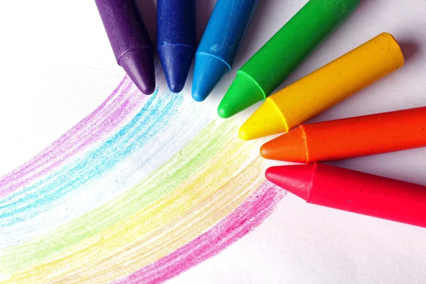 Oil pastel crayons lying on a paper with painted rainbow — Stock Photo, Image