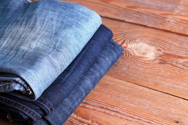 Pilha de jeans azuis e azuis escuros deitados em uma mesa de madeira — Fotografia de Stock