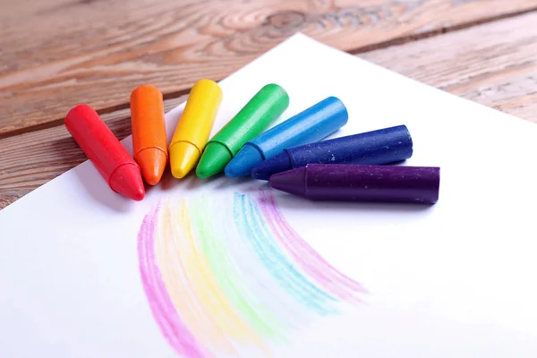 Oil pastel crayons lying on a paper with painted rainbow — Stock Photo, Image