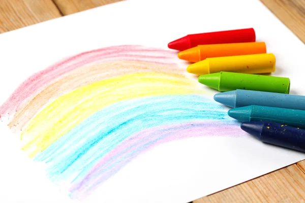 Oil pastel crayons lying on a paper with painted rainbow — Stock Photo, Image