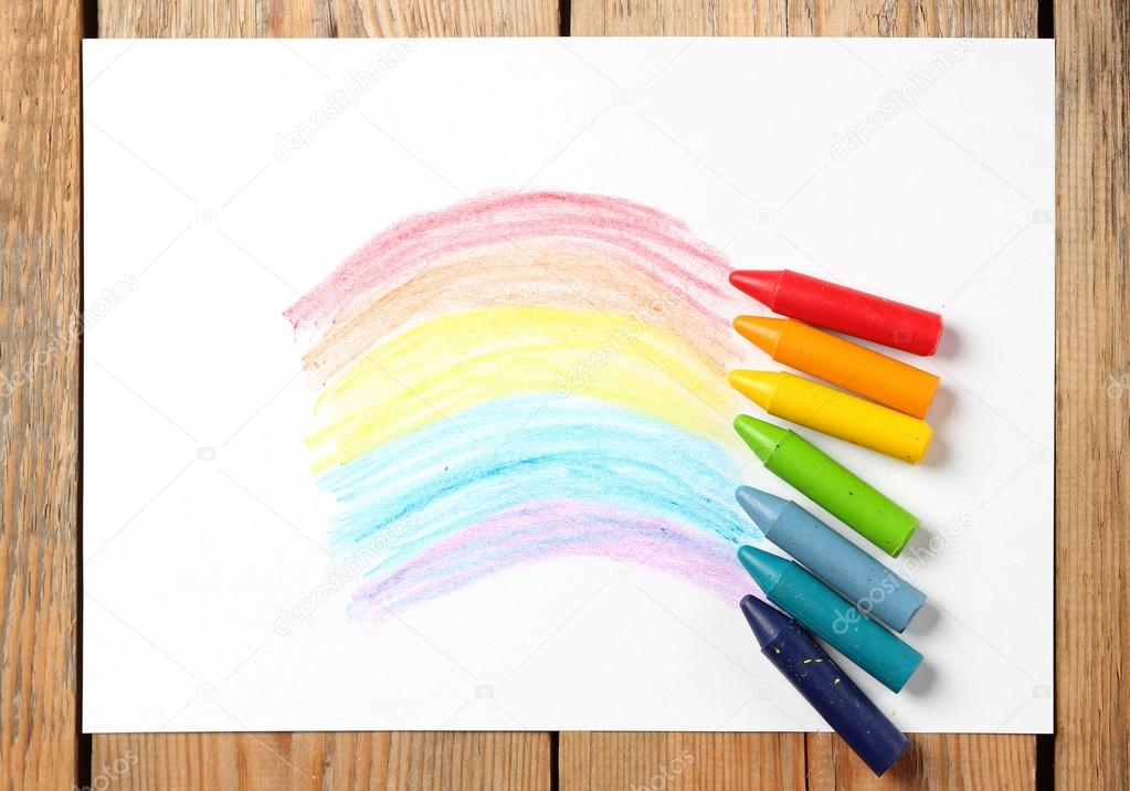 Oil pastel crayons lying on a paper with painted rainbow