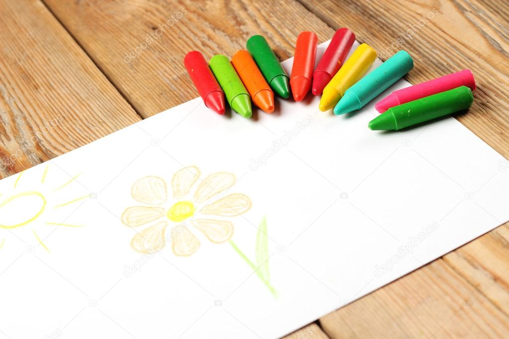 Oil pastel crayons lying on a paper with painted flower and sun