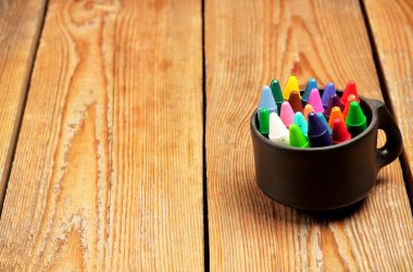 Crayons in a mug on a wooden table clipart