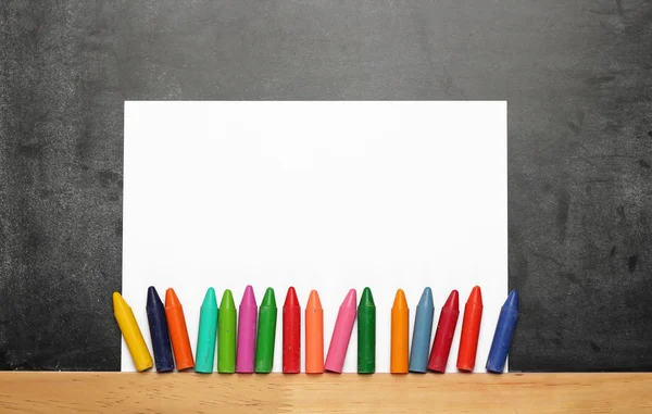 Empty sheet of paper with crayons on a dusty chalkboard — Zdjęcie stockowe