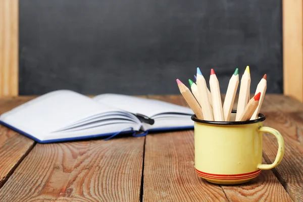 Pencils in a mug, open notebook and chalkboard — Stockfoto
