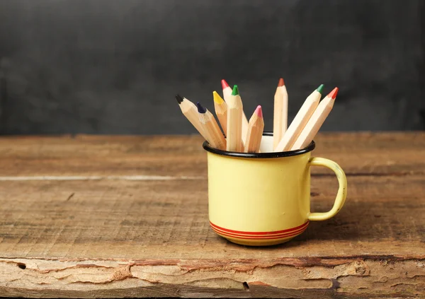 Pencils in a mug on a wooden table and chalkboard — 图库照片