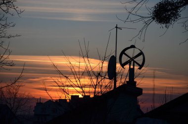 Şehirde gün batımı çok güzeldir. Kızıl gökyüzünün arka planına karşı yuvarlak anten siluetleri.