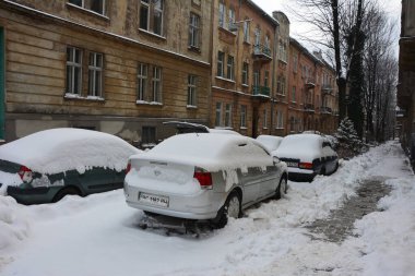 Kar, kış günü kar yağışından sonra arabaları kapladı. Otoparktaki kar fırtınasında araçlar karla kaplandı. Karla kaplı yollar ve şehrin sokakları.