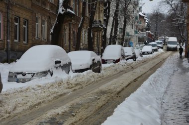 Kar, kış günü kar yağışından sonra arabaları kapladı. Otoparktaki kar fırtınasında araçlar karla kaplandı. Karla kaplı yollar ve şehrin sokakları.