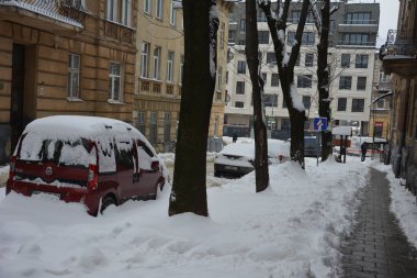 Kar, kış günü kar yağışından sonra arabaları kapladı. Otoparktaki kar fırtınasında araçlar karla kaplandı. Karla kaplı yollar ve şehrin sokakları.