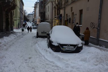 Kar, kış günü kar yağışından sonra arabaları kapladı. Otoparktaki kar fırtınasında araçlar karla kaplandı. Karla kaplı yollar ve şehrin sokakları.