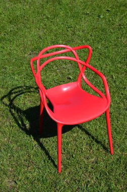 Dinlenmek için çimenlerin üzerinde kırmızı plastik sandalye. Güneşli bir gün. Çimenlerdeki gölgeler sandalyenin şeklini gösteriyor..