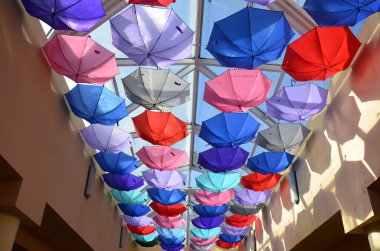 Sergide çok renkli yaz şemsiyeleri sergilenmek üzere askıya alındı. Güneş ışığına sahip bir sürü renkli şemsiye. Mağazanın tavanı müşteri çekmek için gökkuşağı şemsiyeleriyle süslenmiştir...