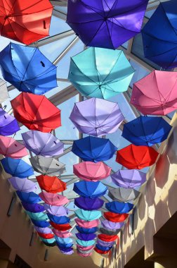 Sergide çok renkli yaz şemsiyeleri sergilenmek üzere askıya alındı. Güneş ışığına sahip bir sürü renkli şemsiye. Mağazanın tavanı müşteri çekmek için gökkuşağı şemsiyeleriyle süslenmiştir...