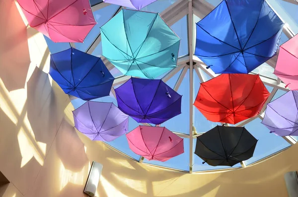 Summer multi-colored umbrellas are suspended for display at the exhibition. Many colorful umbrellas with sunlight. The ceiling in the store is decorated with rainbow umbrellas to attract customers..